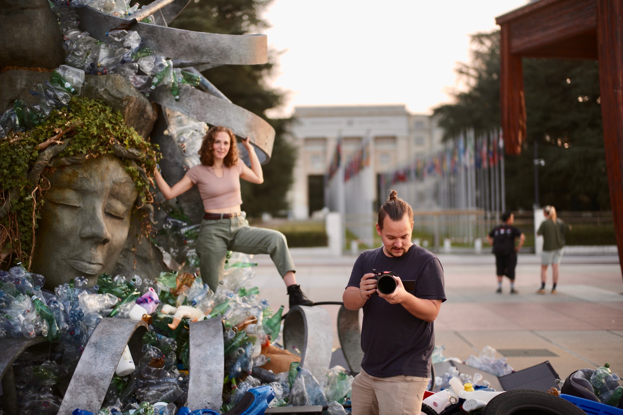 Hope posing atop a sculpture made of plastic waste outside the UN in Geneva while a photographer checks his camera