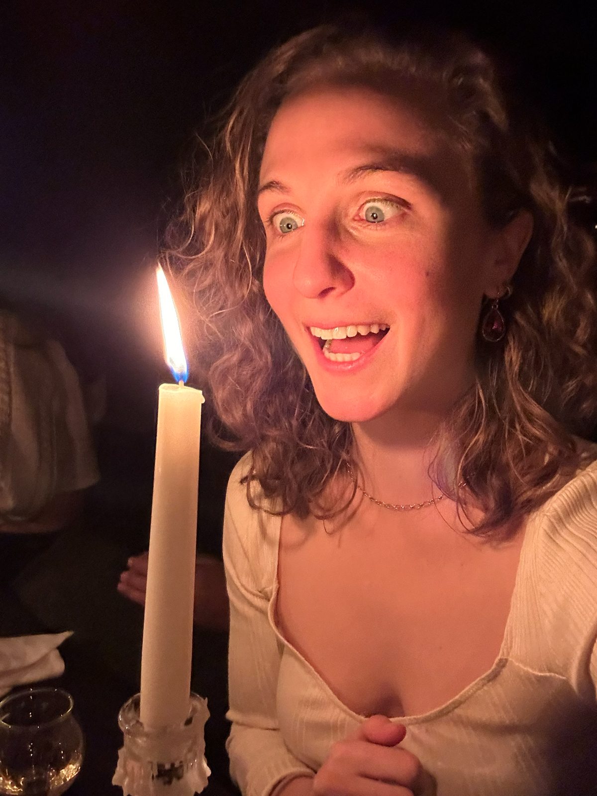 Hope wide-eyed and grinning at a candle flame in a dark room, lit by candlelight