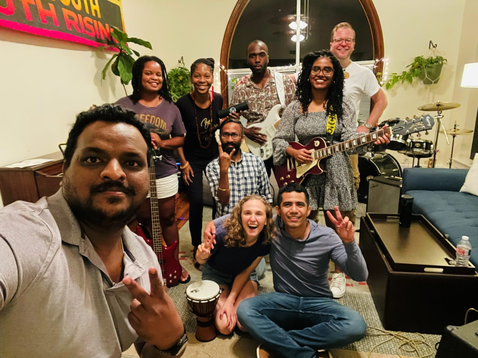 Living-room selfie with friends holding guitars, drums and a djembe, Hope grinning at the front