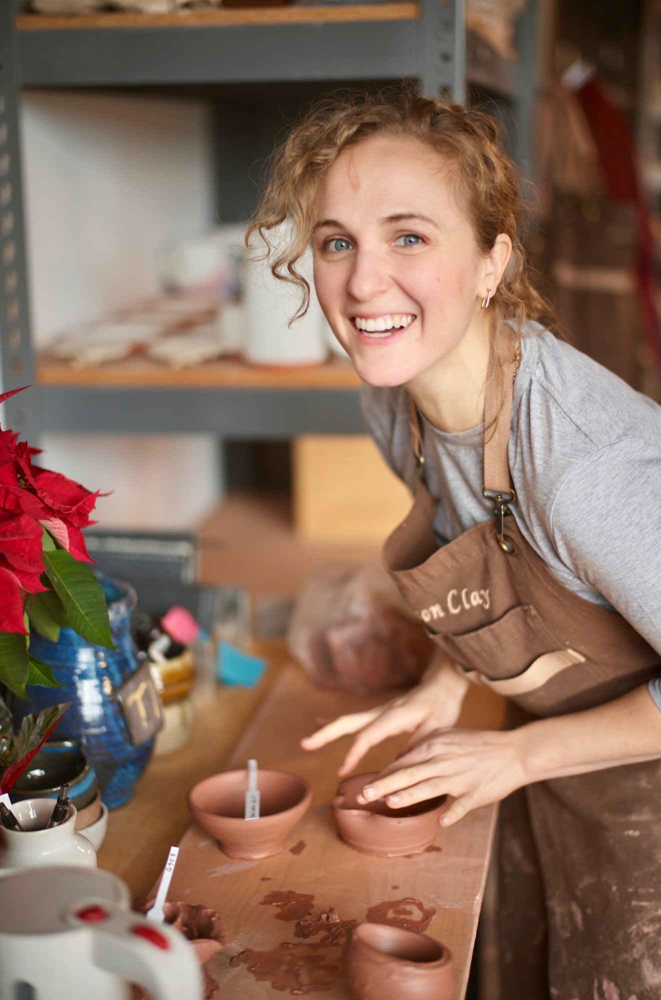 Hope beaming at a pottery studio bench in a clay-smudged apron, shaping a small terracotta bowl