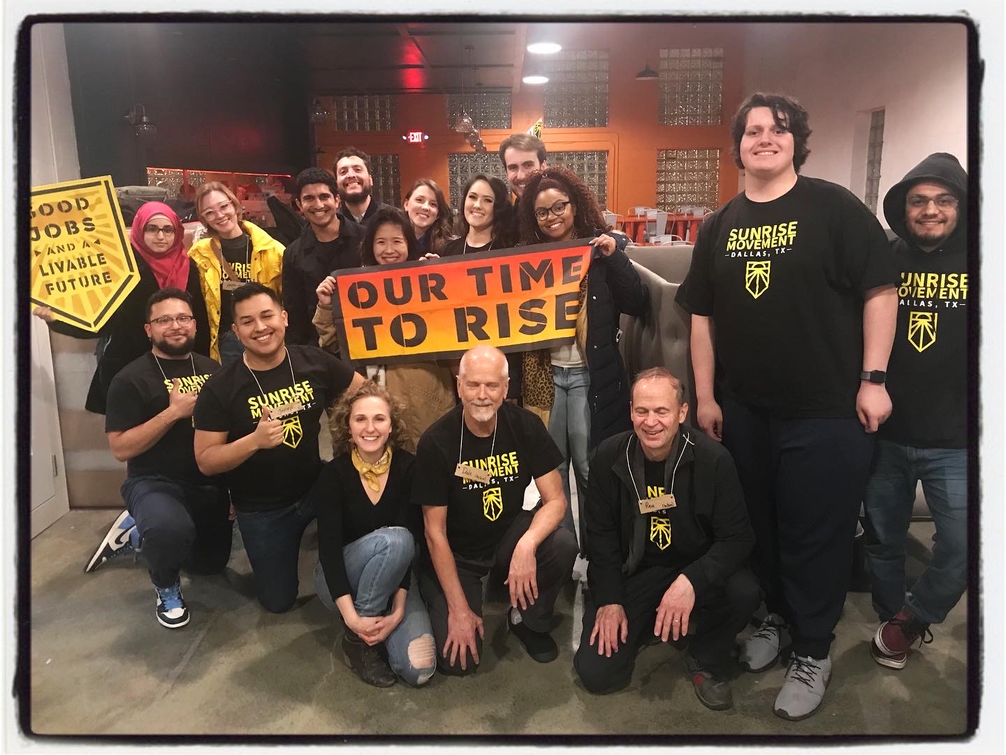 Group photo of the Sunrise Movement Dallas hub holding an Our Time To Rise banner, Hope kneeling at the front