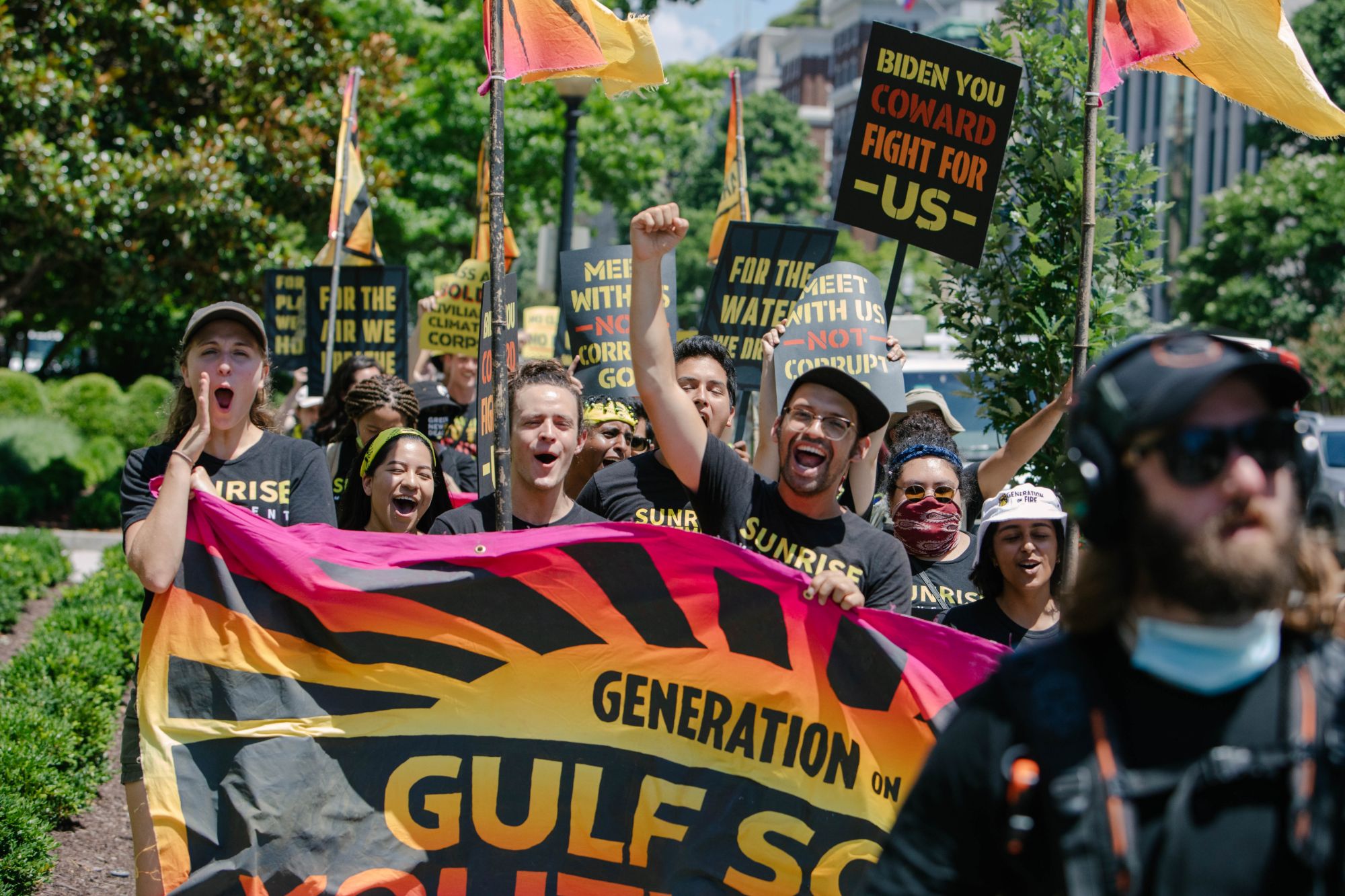 Hope shouting at the front of a Sunrise Movement march in Washington DC, holding a Generation on Fire banner with fellow organizers under orange flags