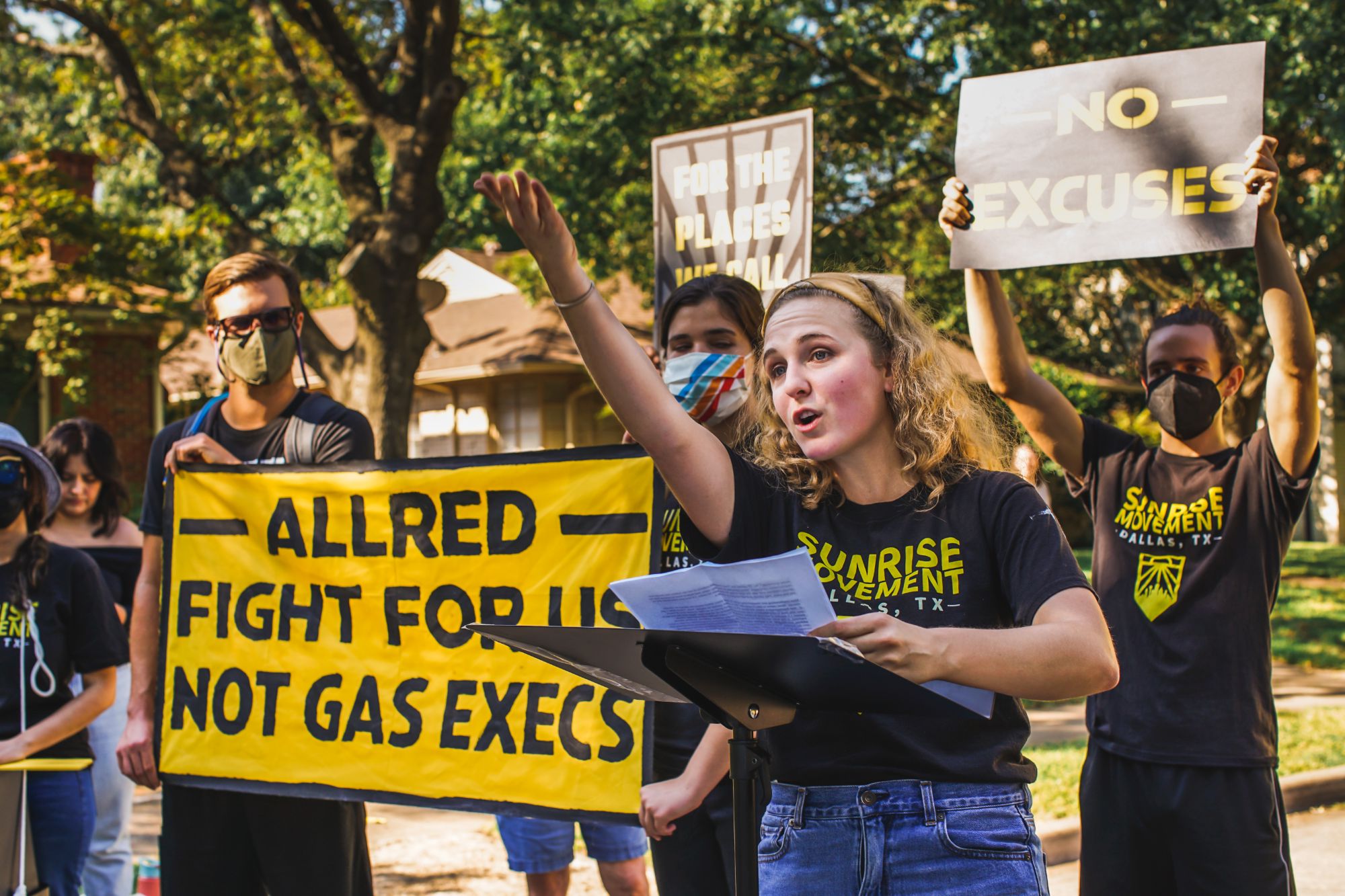 Hope speaking at a lectern with a raised fist at a Sunrise Movement rally, banner reading Allred fight for us not gas execs