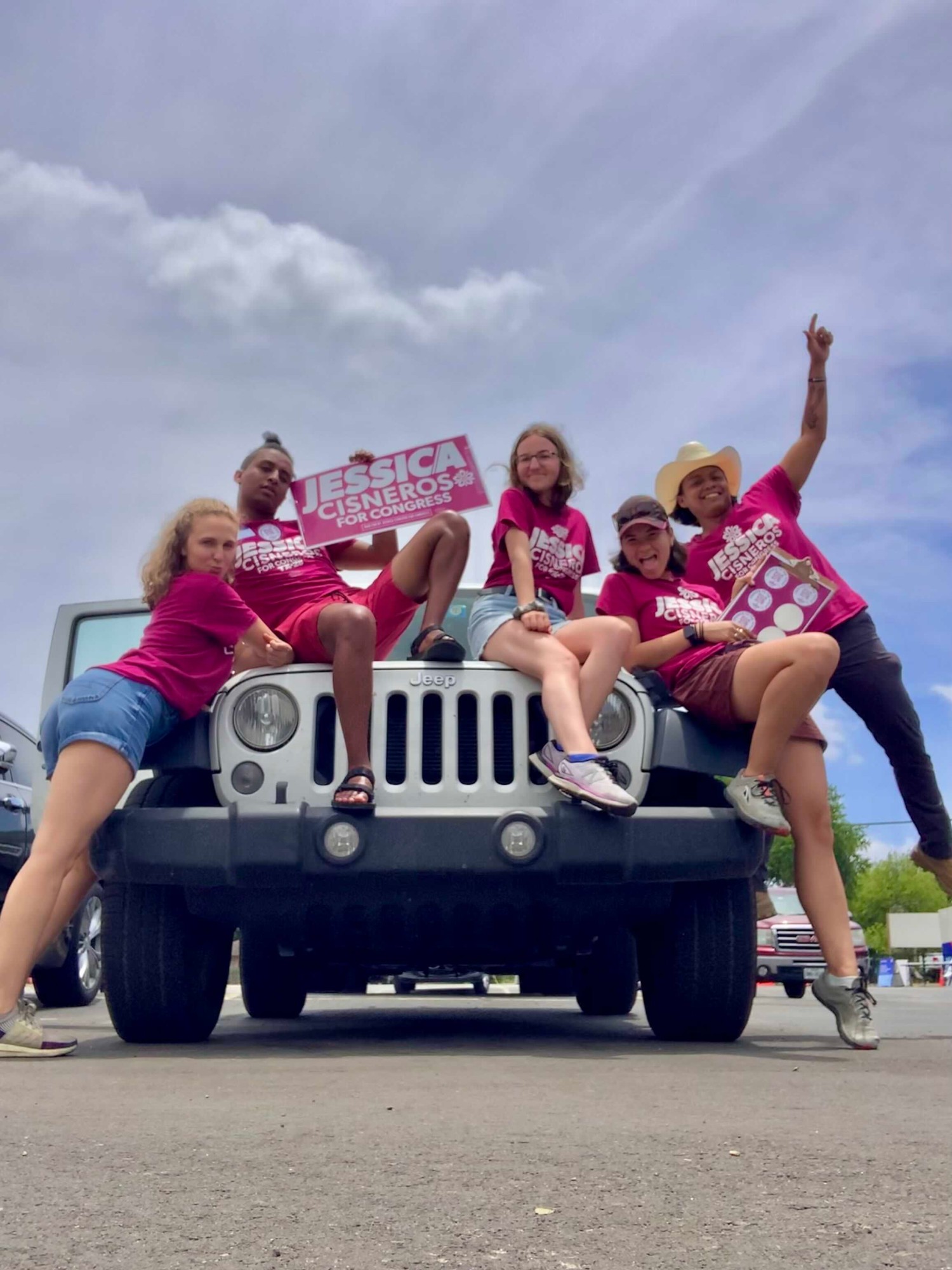Hope and four campaign volunteers in pink Jessica Cisneros for Congress shirts striking playful poses on the front of a Jeep