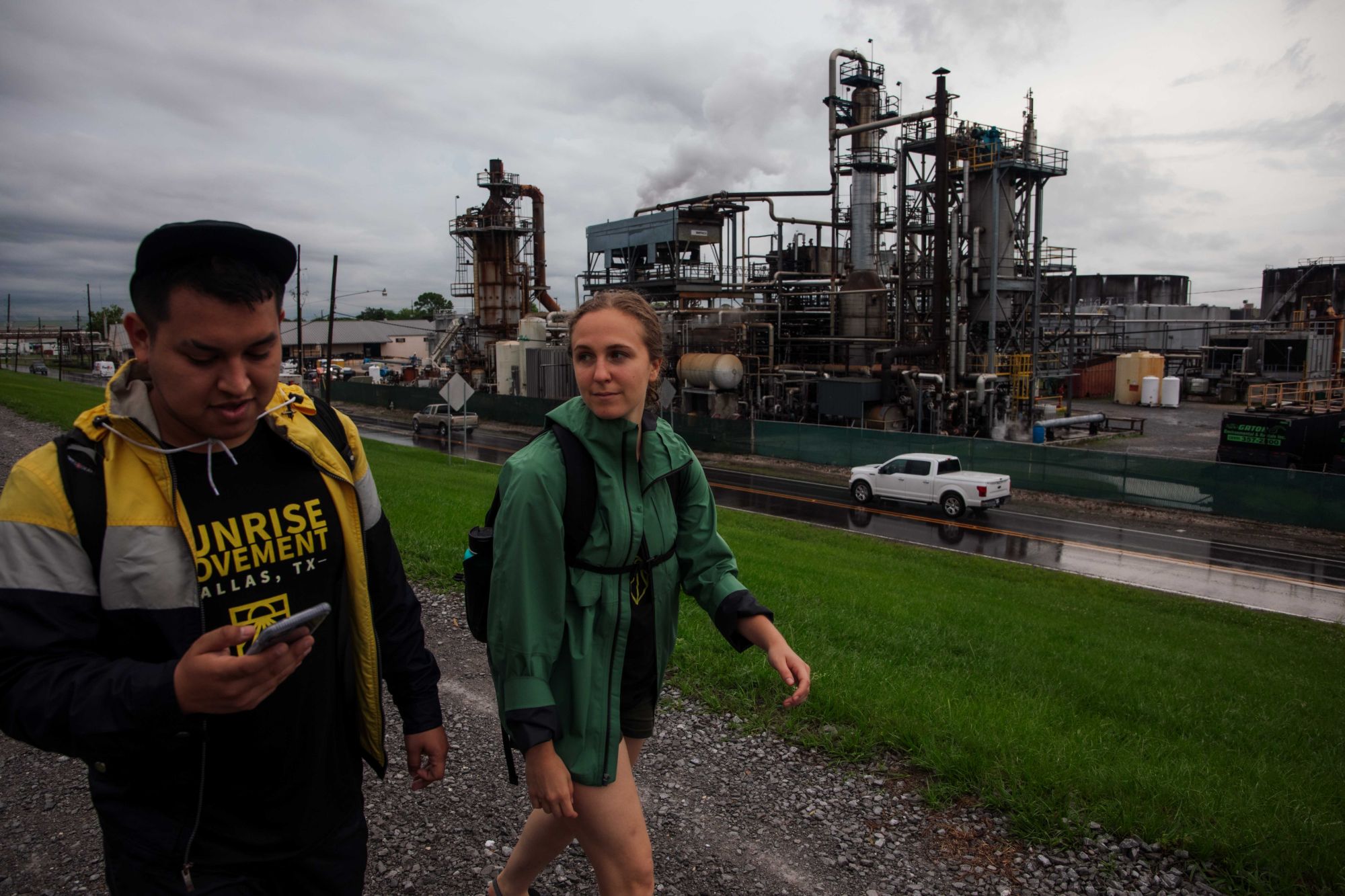 Hope in a green rain jacket walking past a petrochemical plant with a fellow Sunrise marcher on the Gulf South March