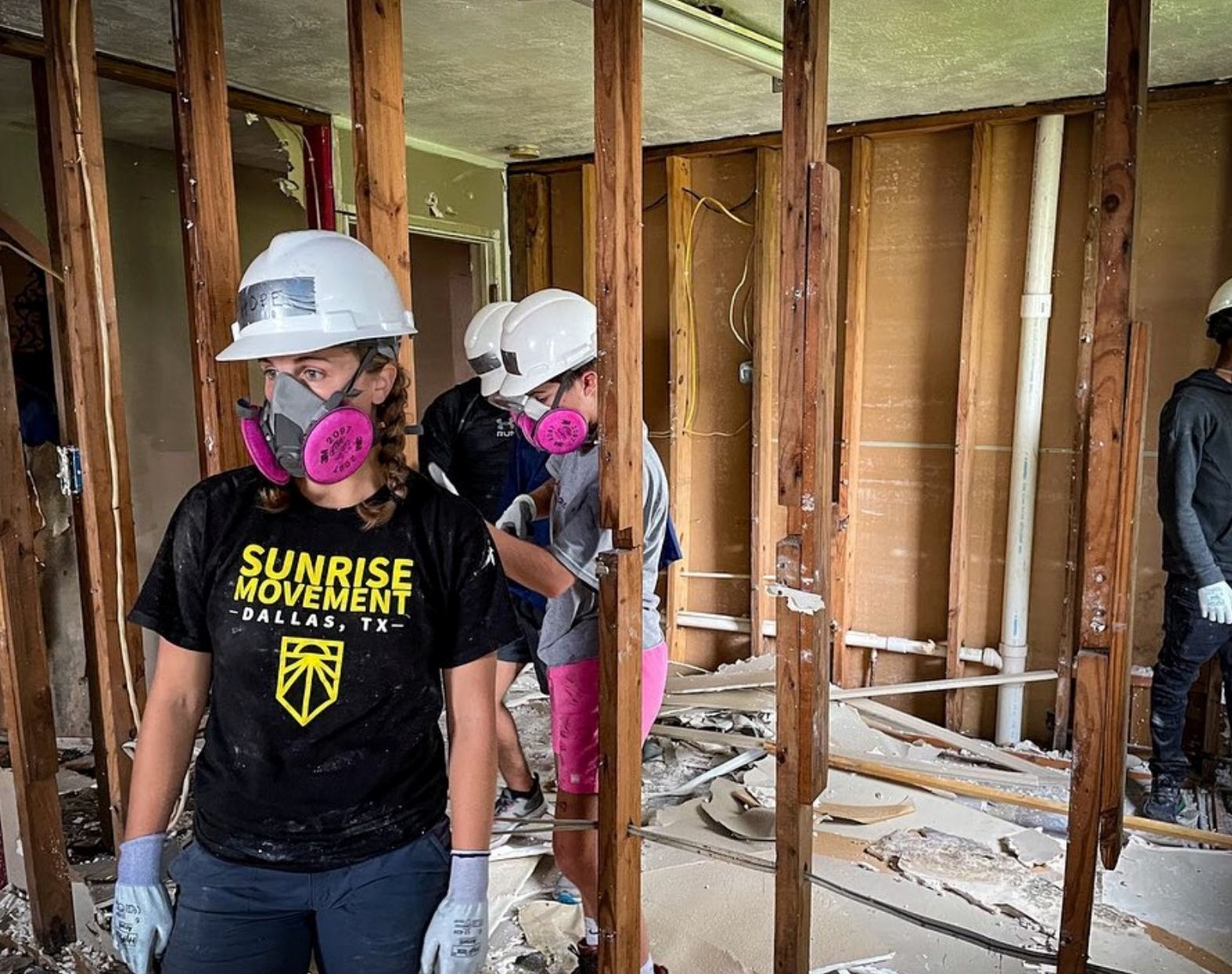 Hope in a hard hat, respirator and work gloves inside a gutted house stripped to the studs, with fellow volunteers behind her
