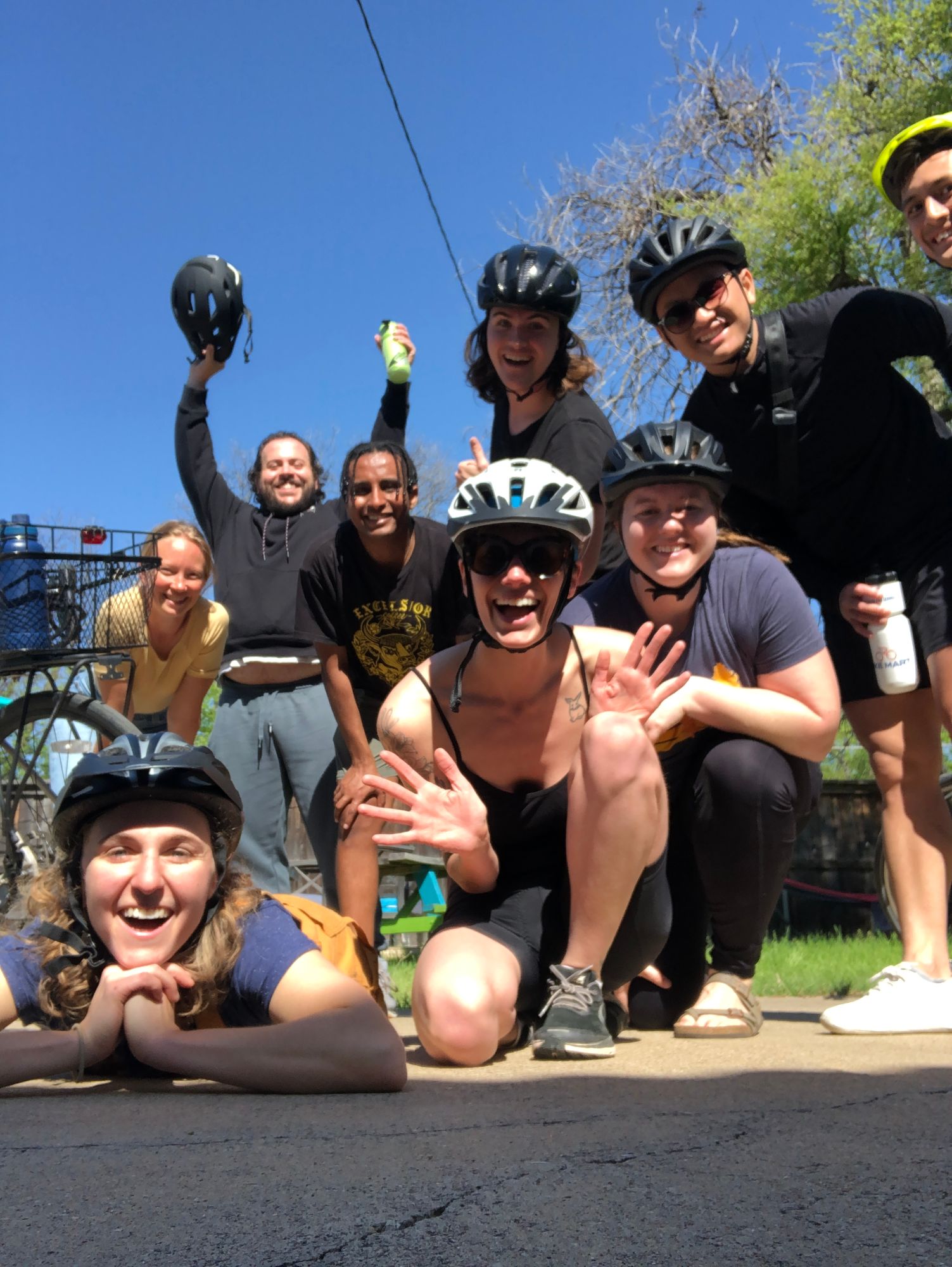 A group of friends in bike helmets posing on a sunny street, Hope lying at the front with her chin in her hands