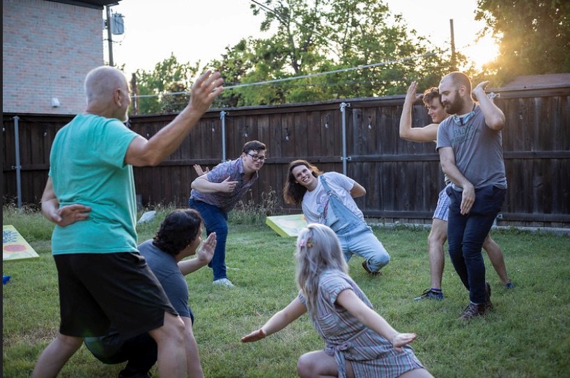 Six friends mid-game in a backyard at golden hour, crouching and lunging with arms out on the grass