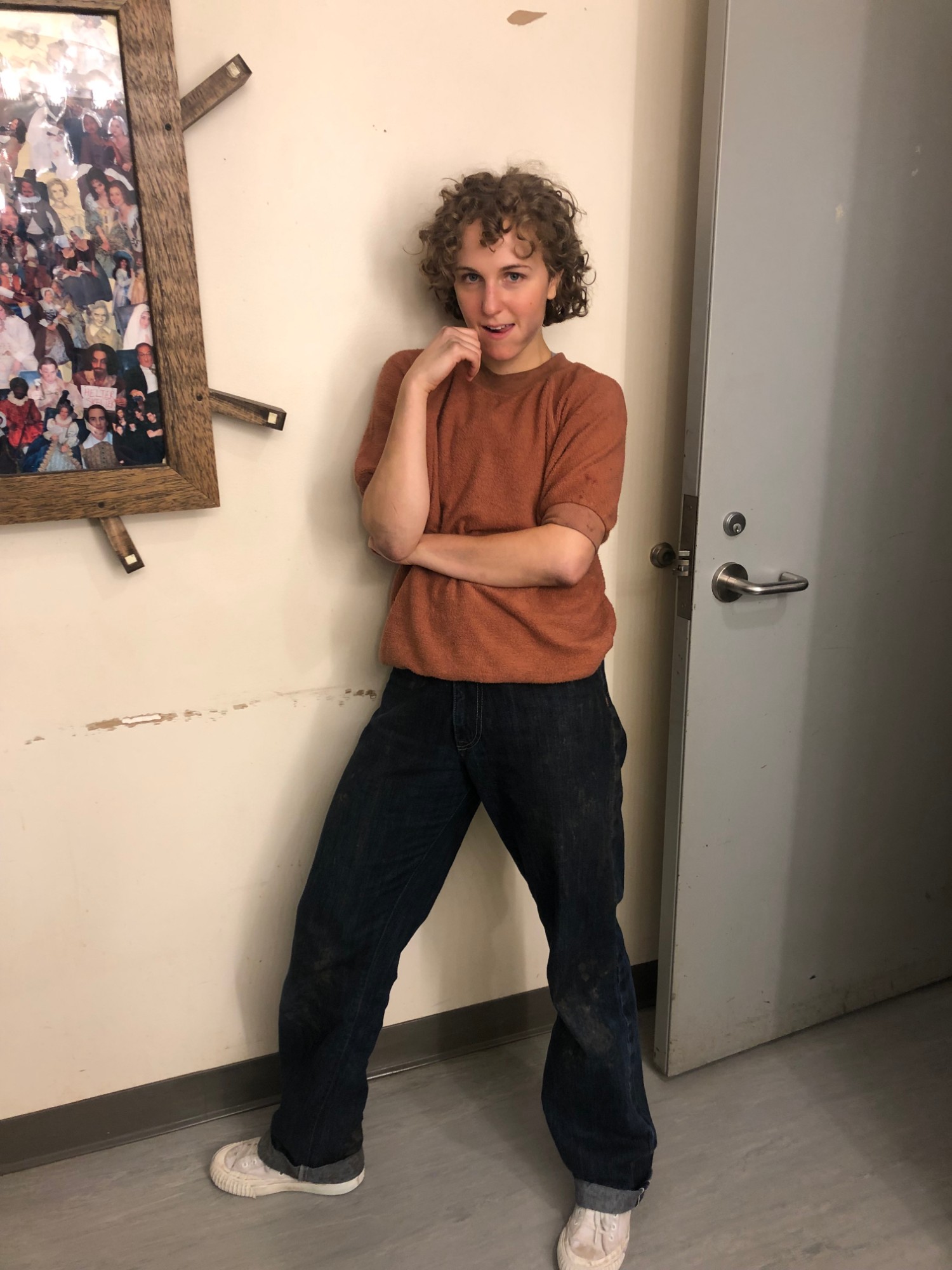 Hope in costume as Anybodys, short curls, rust sweatshirt and jeans, leaning against a backstage wall