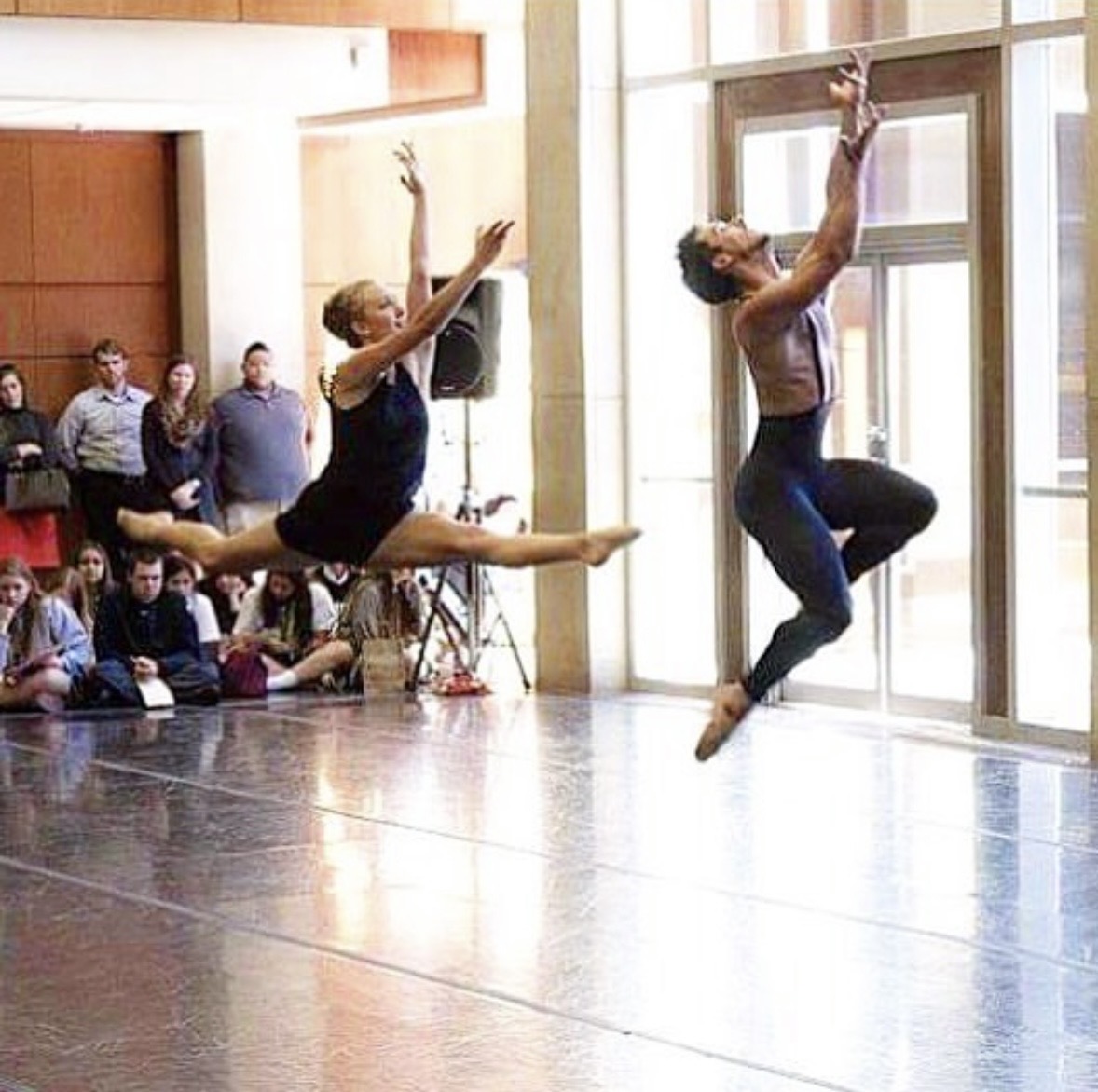 Hope mid-leap in a split jump beside a dance partner, performing a duet in a sunlit studio