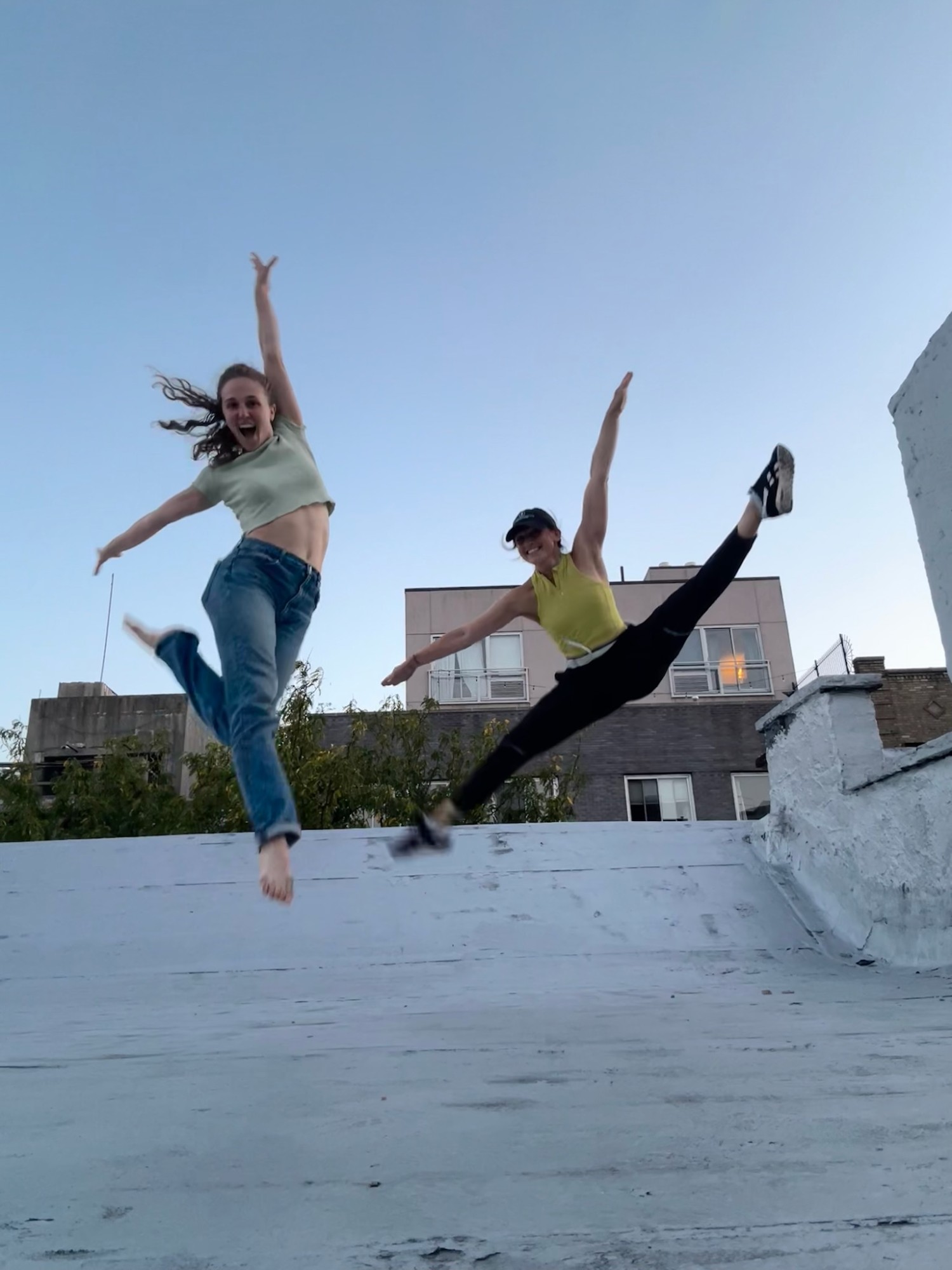 Hope and her roommate leaping mid-air on a rooftop against a blue evening sky