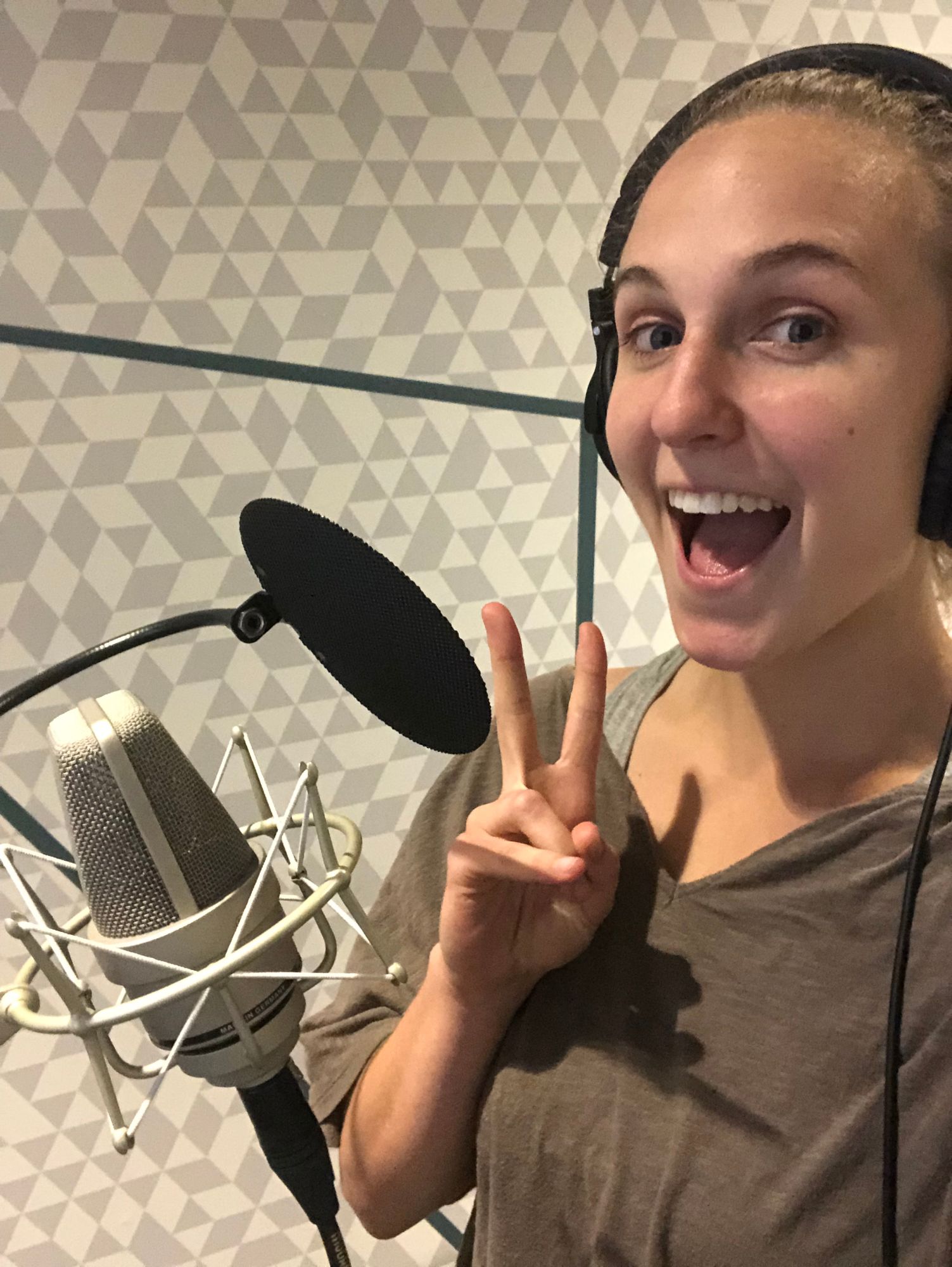 Hope in headphones at a studio microphone, grinning and flashing a peace sign