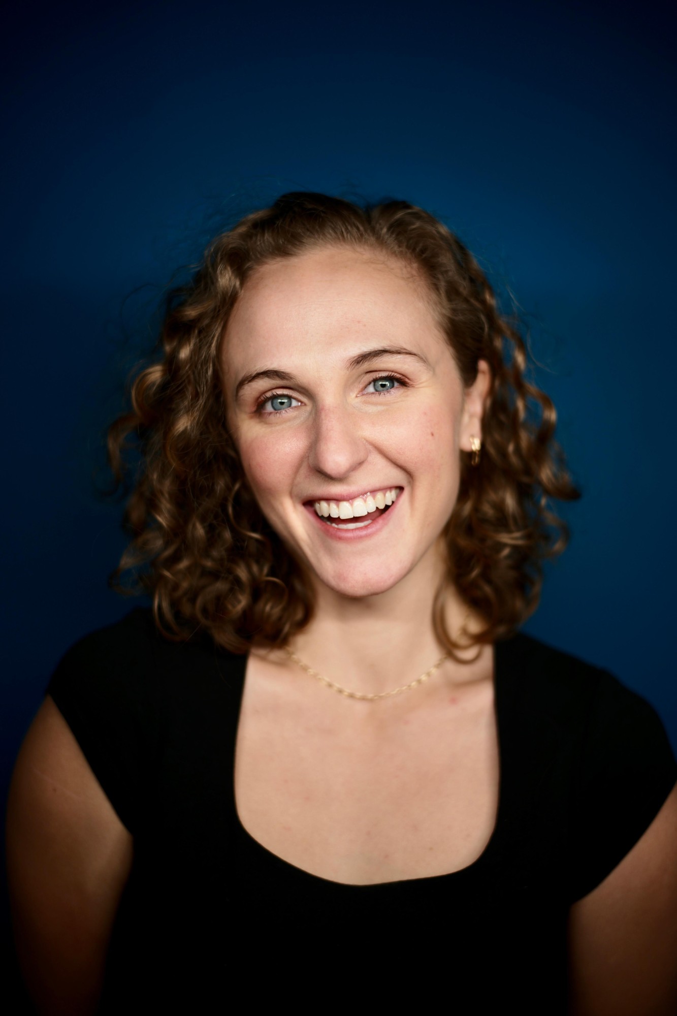 Hope smiling, curly hair, black top, deep blue background